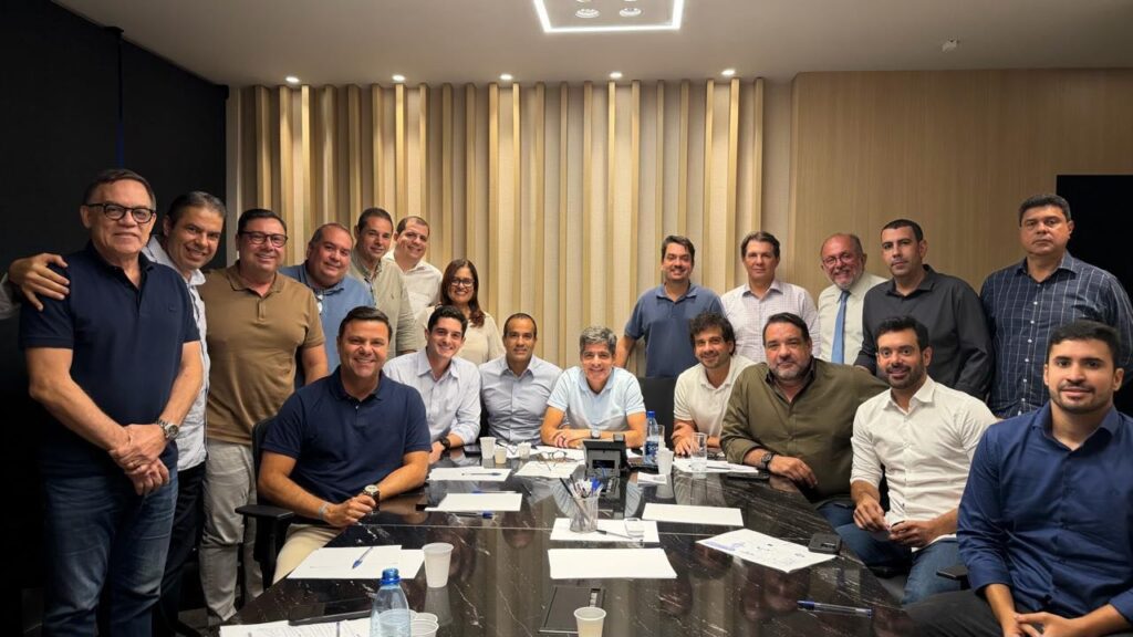 ACM Neto sentado à mesa durante reunião com deputados e lideranças políticas, todos reunidos em um ambiente interno para discutir estratégias eleitorais.