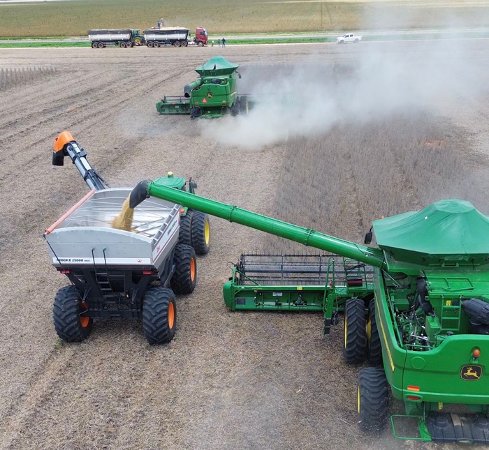 Máquinas agrícolas colhendo soja em lavoura no Cerrado da Bahia, com poeira levantada ao fundo indicando ritmo intenso de colheita.
