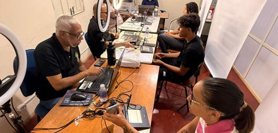Atendimento itinerante do TRE-BA com eleitores sendo atendidos em sala equipada com computadores e equipamentos para biometria