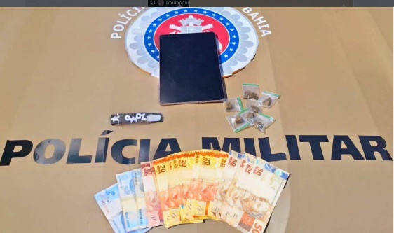 Policiais militares ao lado de materiais apreendidos, incluindo tablet, drogas e dinheiro em Cristópolis